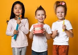 Three small children holding toothbrushes and a mold of a mouth