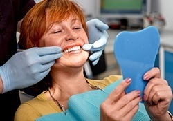 Older woman in dental chair looking at smile in mirror