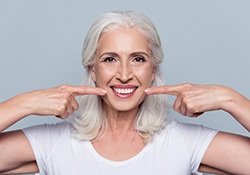 Woman with dentures pointing to her smile