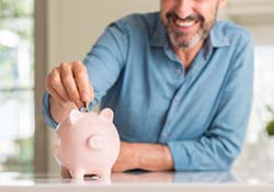 Man placing a coin into a glass piggy bank