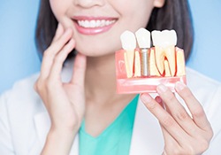 dental implant dentist in New Lenox holding a model of a dental implant 