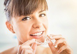 Smiling woman with brown hair holding her Invisalign in New Lenox