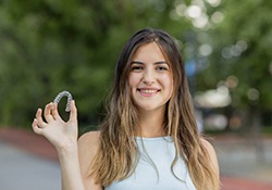 Smiling woman holding Invisalign outside