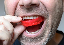 man putting a red mouthguard into his mouth 