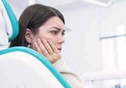 Woman in dental chair holding cheek