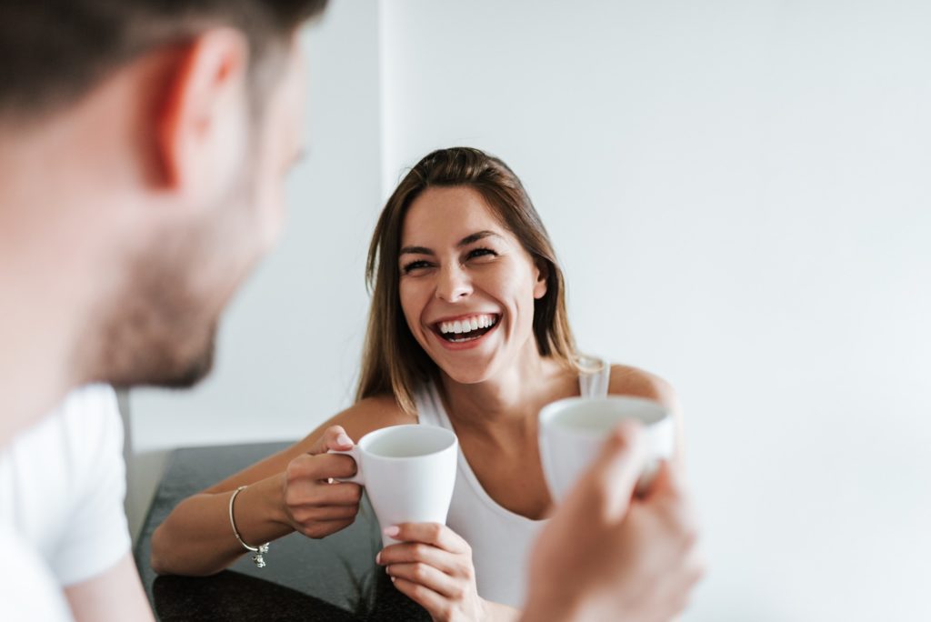 Woman smiling while enjoying cup of coffee with friend