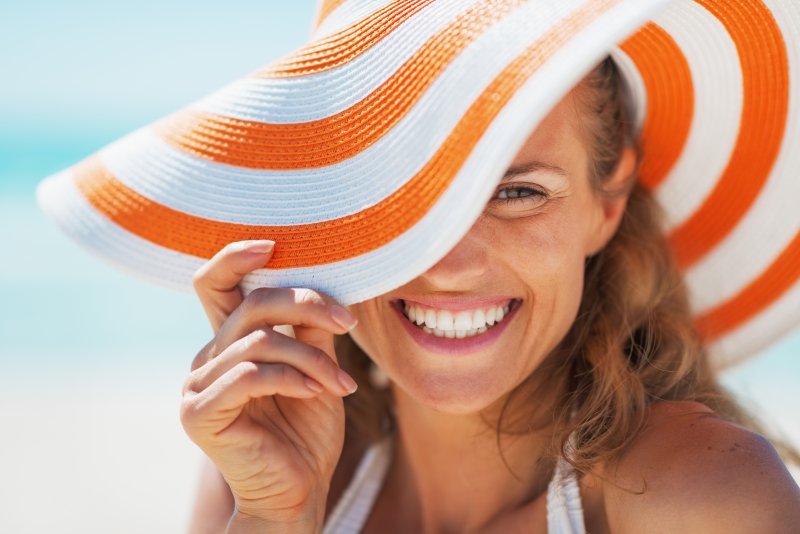 Woman smiles wearing beach hat.