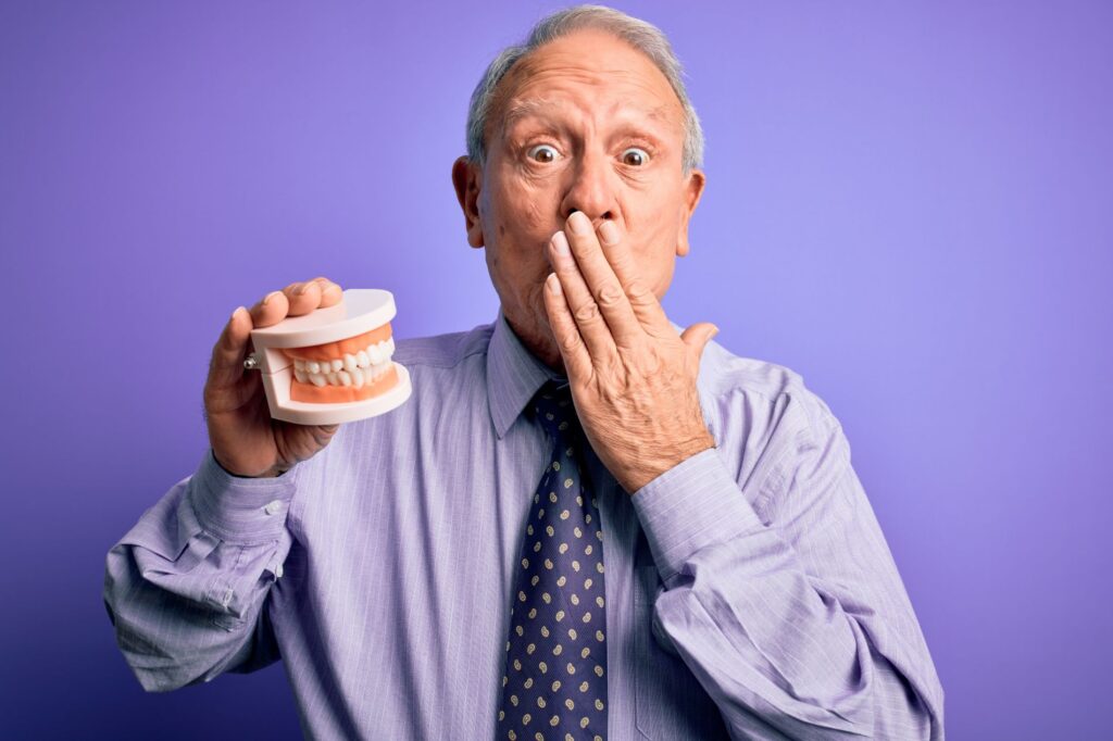 A man covering his mouth and holding dentures